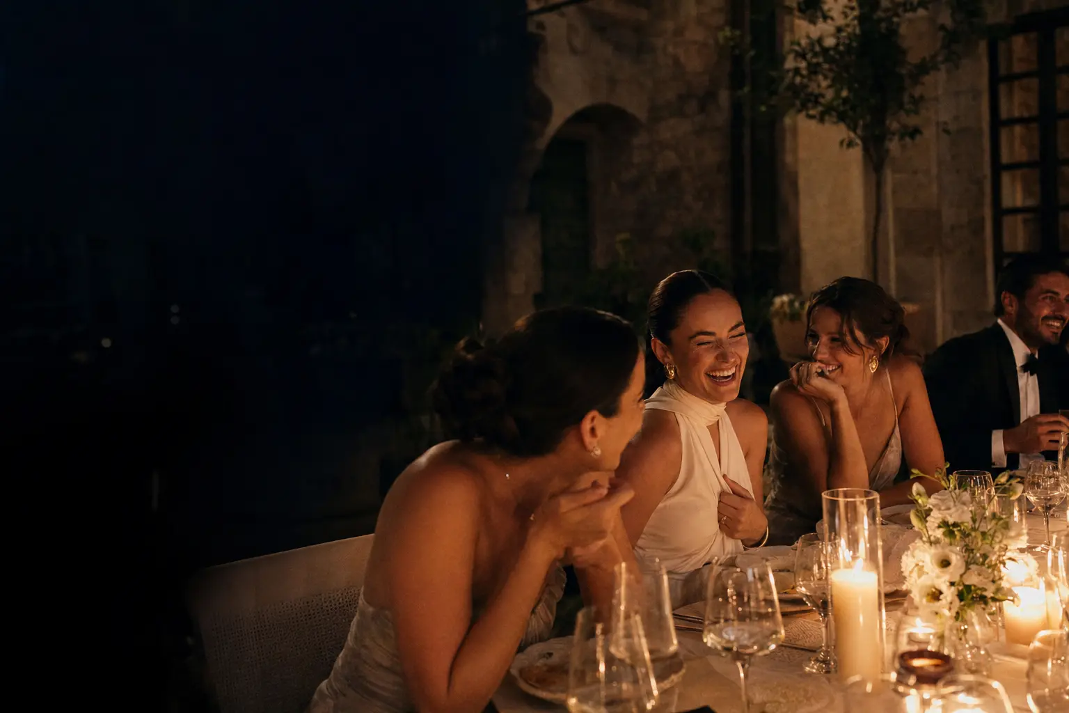 Friends laughing together at a candlelit wedding dinner